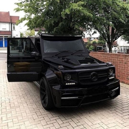 a black mercedes g class parked in front of a brick wall