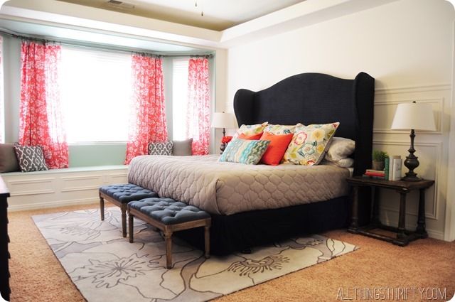 a bedroom with a large bed and red drapes on the windowsill, along with an ottoman