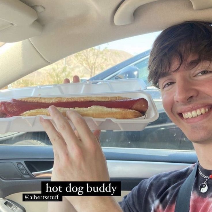 a man sitting in a car holding a hot dog with mustard and ketchup