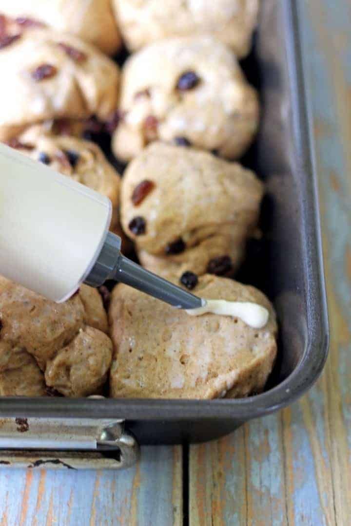 someone is spreading icing onto some cookies in a pan on a wooden table with other pastries