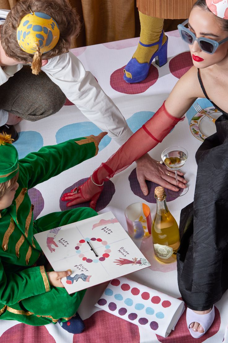 three children dressed up in costumes sitting at a table with cards and bottles on it