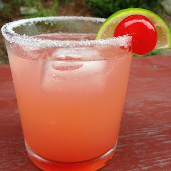 a pink drink with a lime and a cherry on the rim