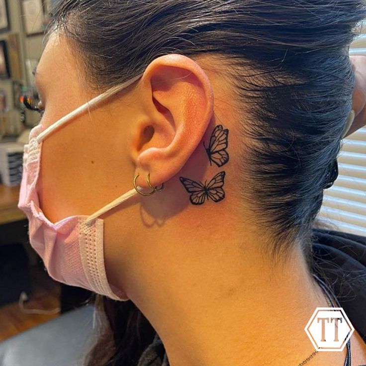 a woman with a butterfly tattoo on her left side behind the ear is wearing a face mask