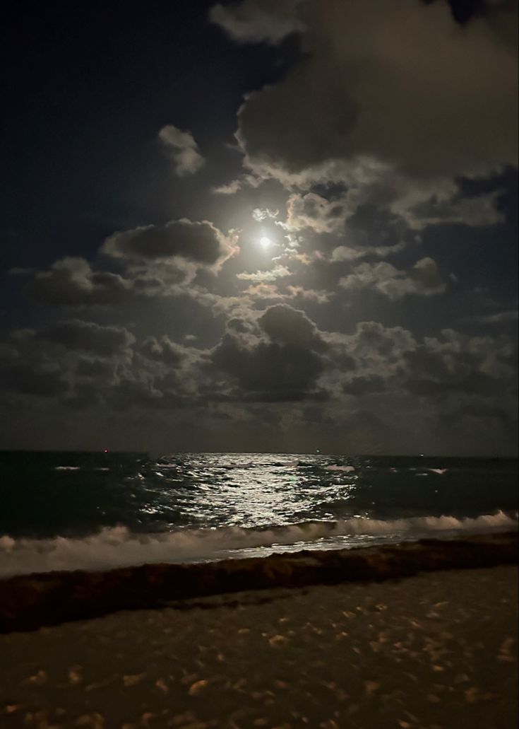 the moon shines brightly over the ocean on a cloudy night