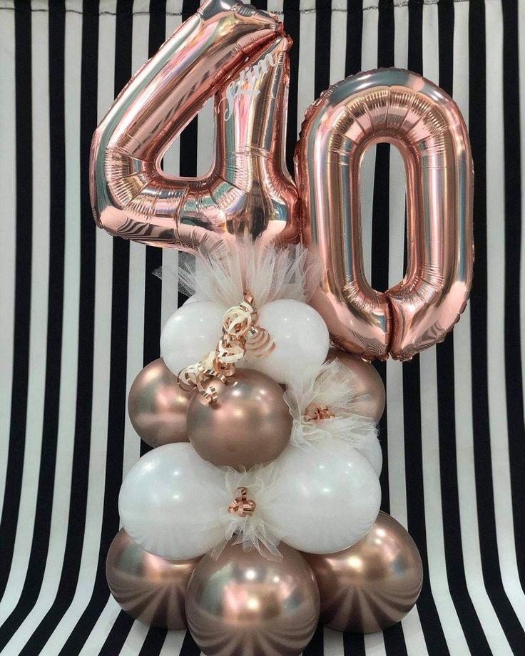 the number forty balloon is placed on top of some white and gold balloons in front of a black and white striped background