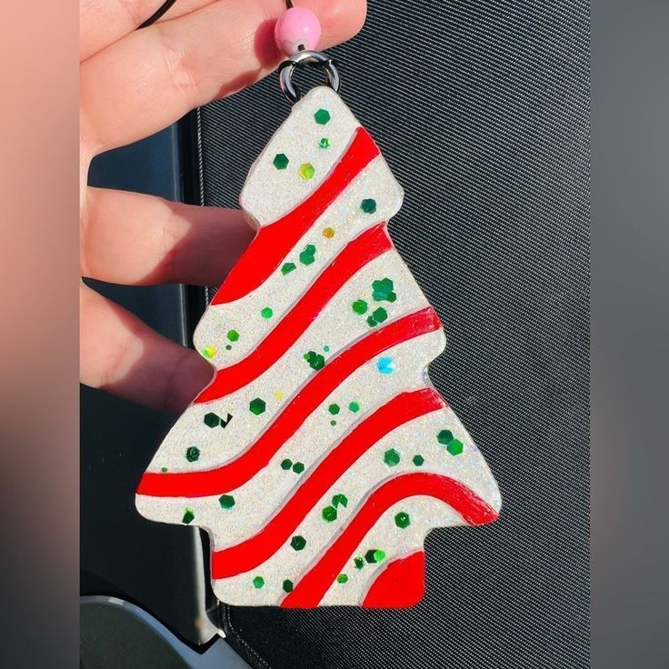 a hand holding a red and white christmas tree ornament with green dots on it