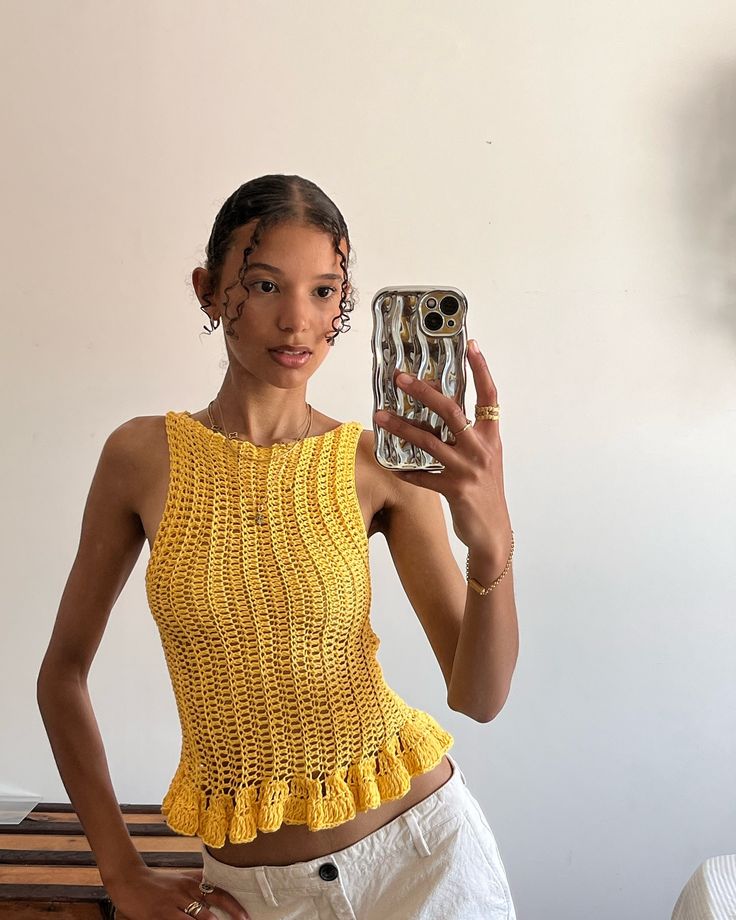 a woman taking a selfie with her cell phone in front of her face and wearing a yellow crop top