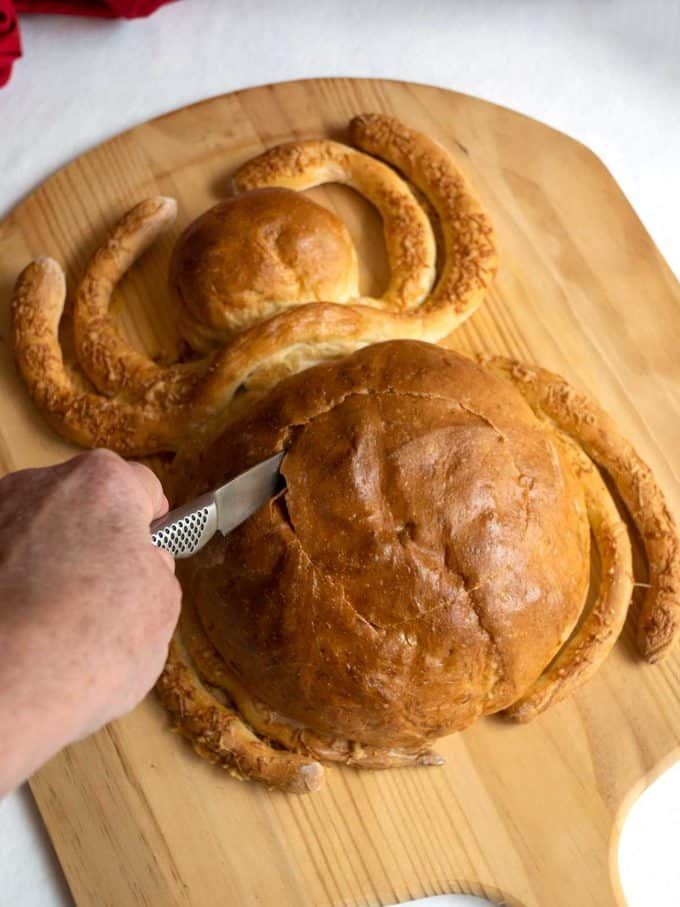 a wooden cutting board topped with rolls and a person using a knife to cut them