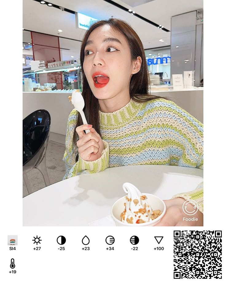 a woman eating ice cream with a spoon in her hand while sitting at a table