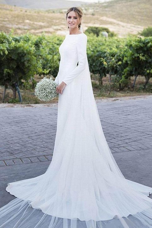 a woman in a white wedding dress standing on a brick road with trees and bushes behind her