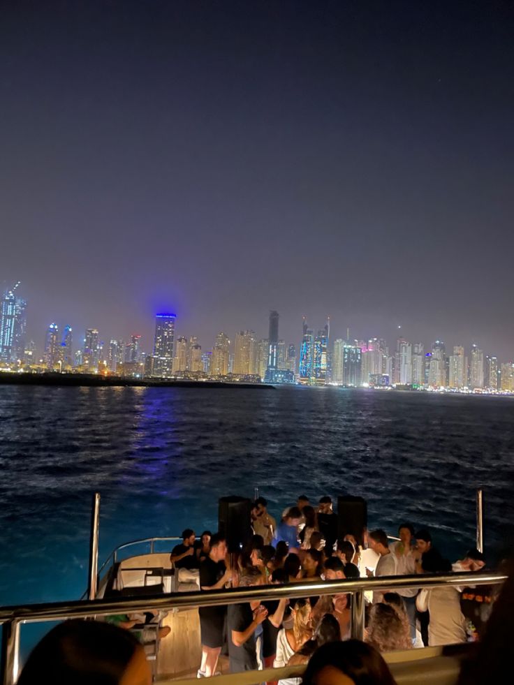 people are sitting on the back of a boat in the water with city lights behind them