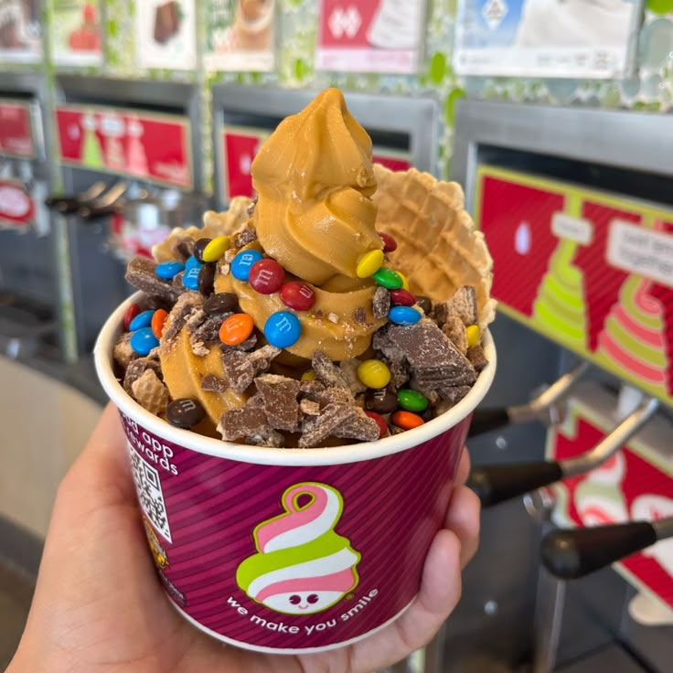 a person holding up a cup filled with chocolate and candy cereal ice cream in a store