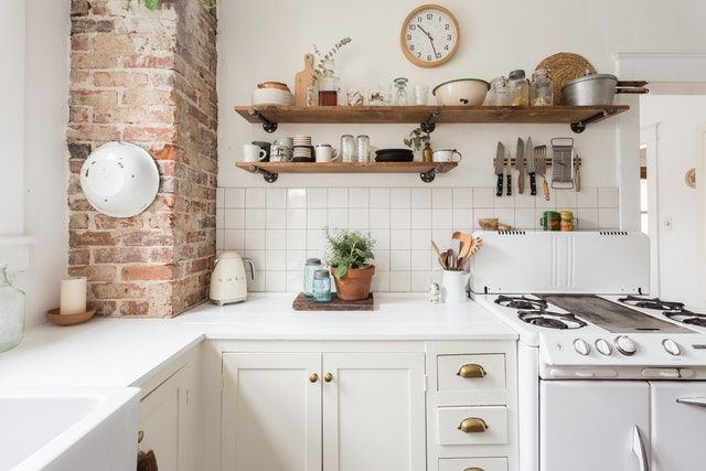 a kitchen with brick wall and white cabinets, open shelving above the stove is filled with pots and pans