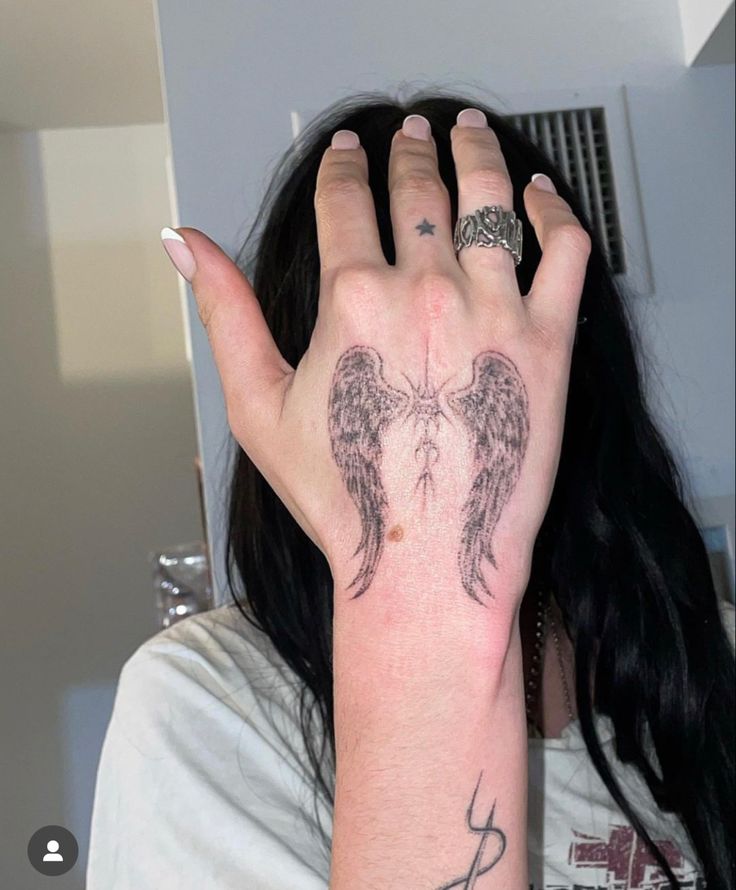 a woman's hand with an angel tattoo on her left wrist and two black wings