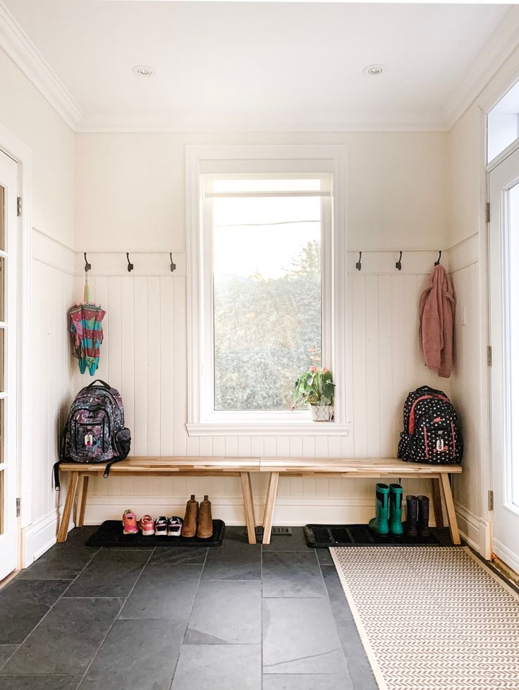 there is a bench in the room with two bags on it and shoes under the window