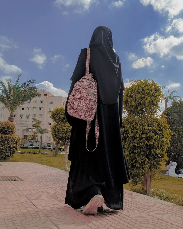 a woman with a backpack walking down the street in front of some trees and buildings