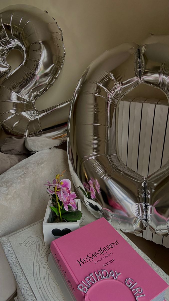 a pink book sitting on top of a table next to some silver balloons and flowers