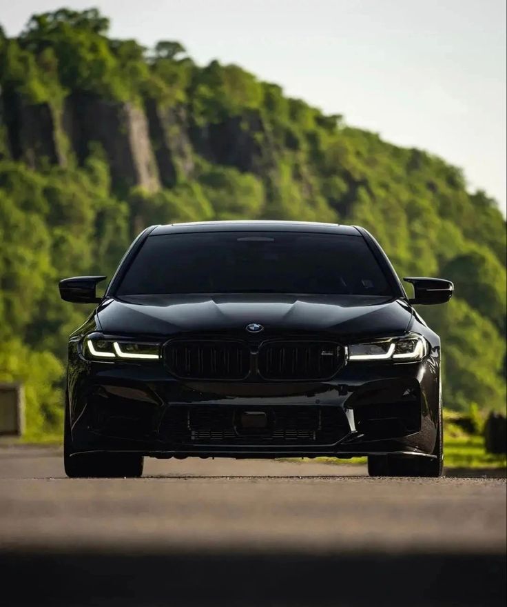 the front end of a black bmw car parked in front of a green mountain range