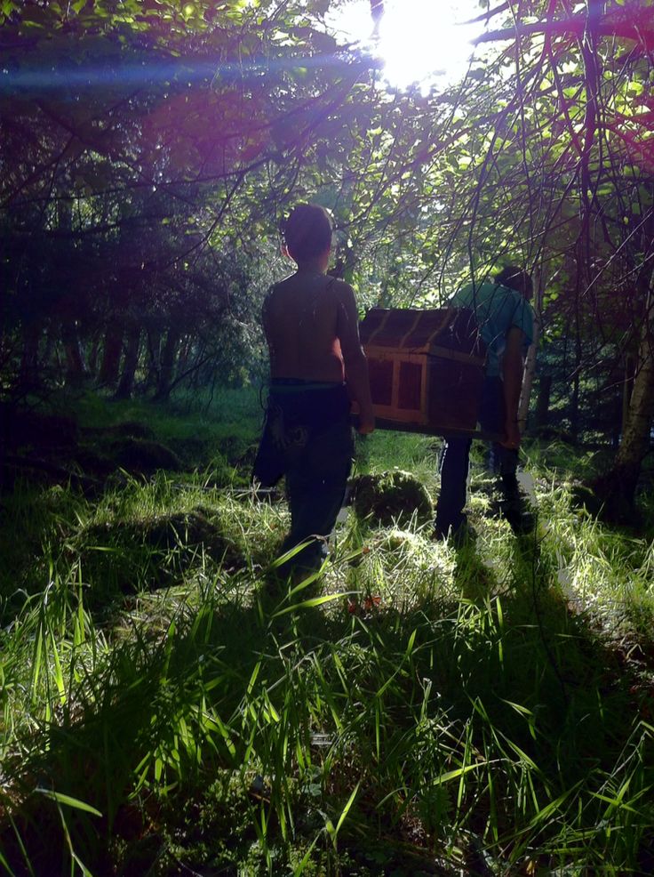 two people standing in the woods with a wooden box on their back and one person carrying something behind them