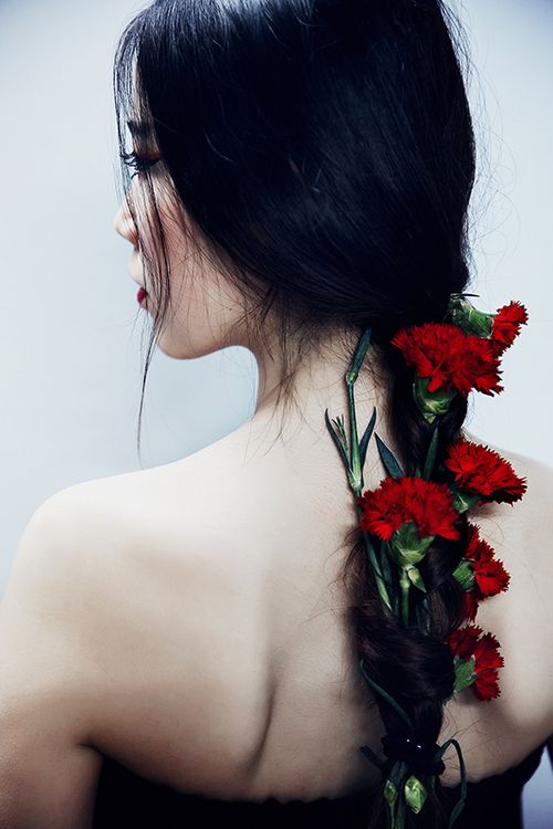 the back of a woman's head with red flowers in her hair and braid