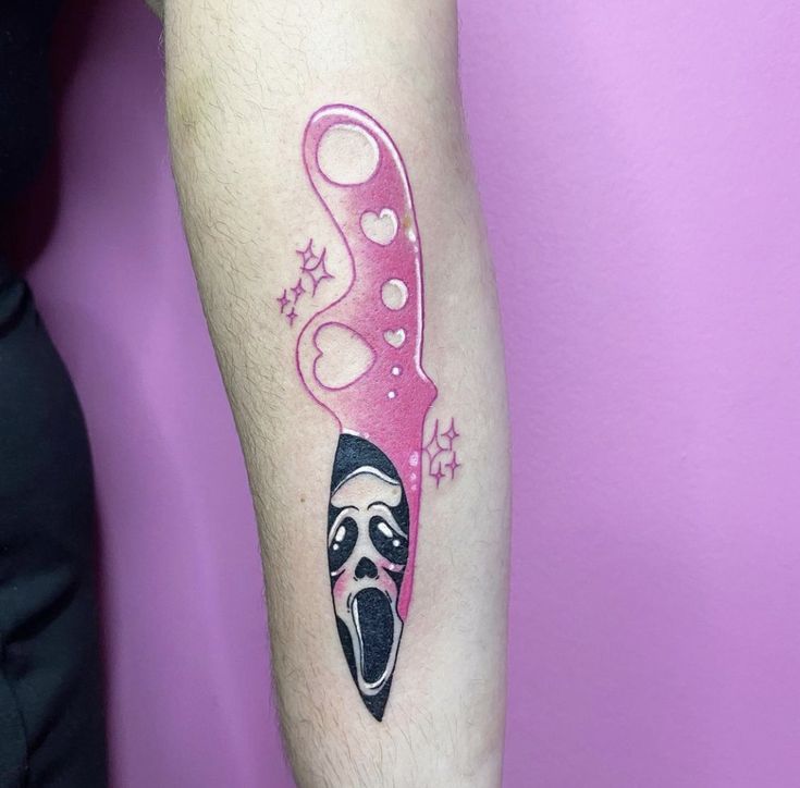 a woman's arm with a pink and black mask tattoo on the left forearm