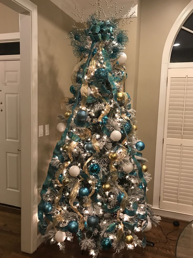 a blue and silver christmas tree with ornaments on it's base in a living room