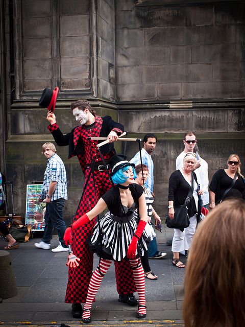 two people dressed as clowns performing on the street in front of a group of people