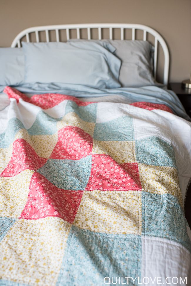 a bed with a quilt on top of it and a pillow in the corner next to it