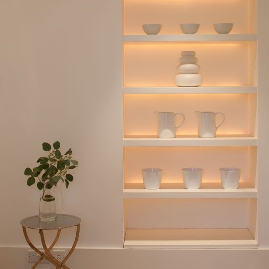 a white shelf with cups and vases on it next to a small glass table