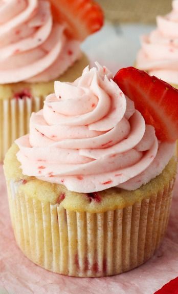 three cupcakes with pink frosting and strawberries on top, sitting on a red napkin