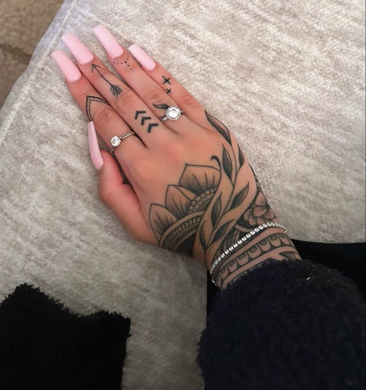 a woman's hand with tattoos on her left arm and fingers, sitting on a couch