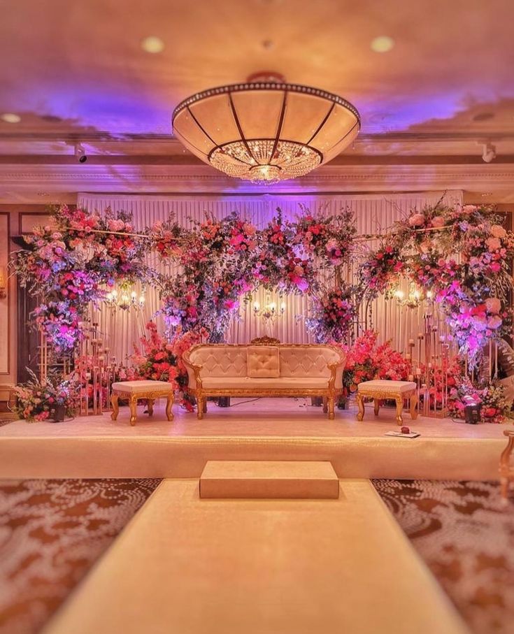 a room decorated with flowers and couches in front of a chandelier filled with candles