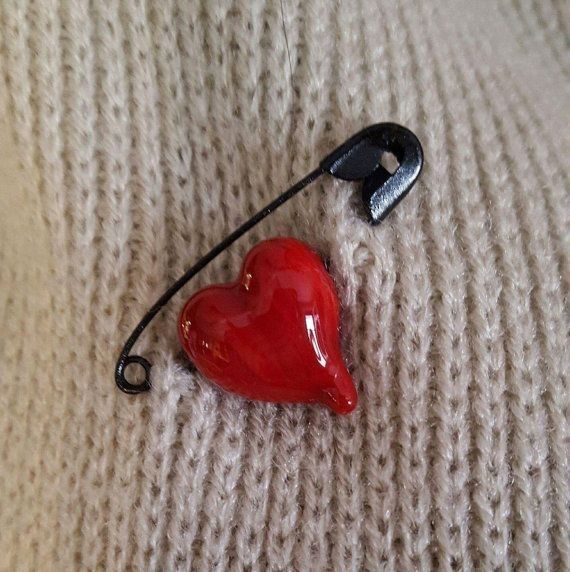 a red heart shaped brooch sitting on top of a white sweater