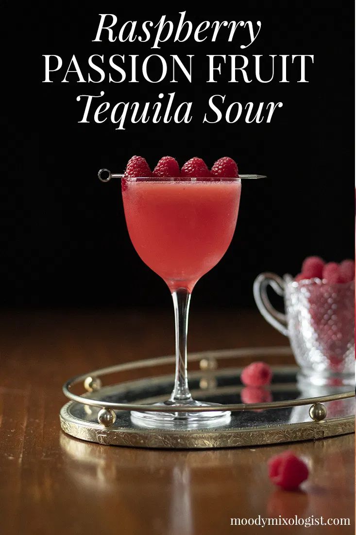 raspberry passion fruit tequila sour in a coupe glass on a tray with raspberries