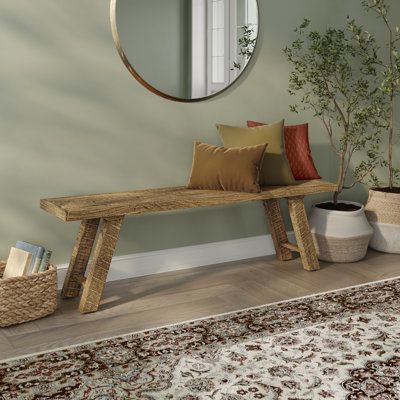 a wooden bench sitting in front of a mirror next to a rug and potted plant