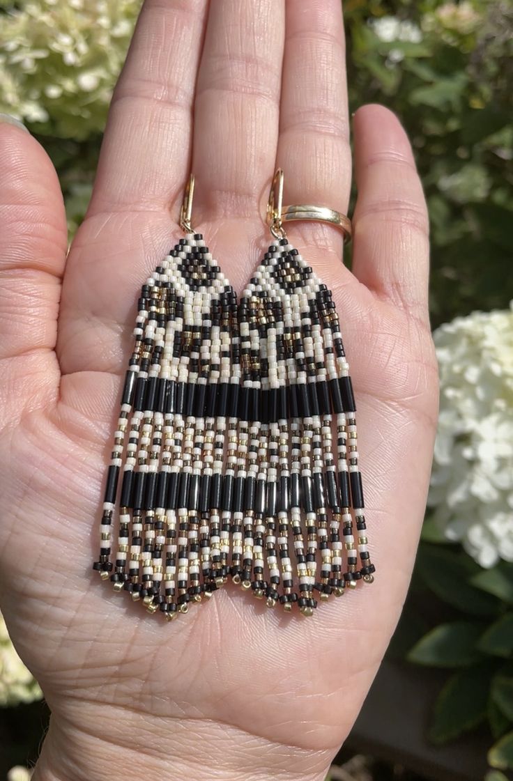 a hand holding a pair of beaded earrings in front of some white and brown flowers