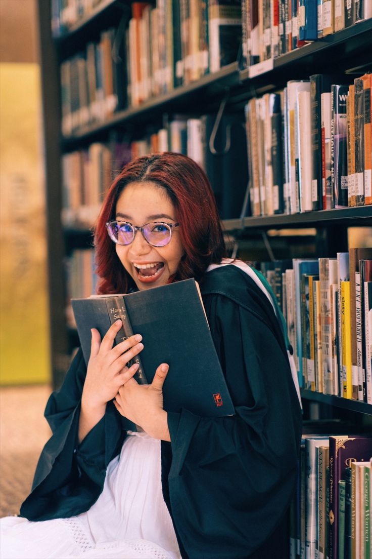 a woman sitting on the ground in front of a bookshelf holding a book