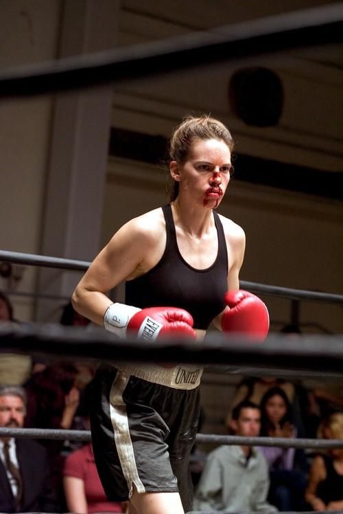 a woman in black shirt and red boxing gloves standing next to a metal ring with people watching