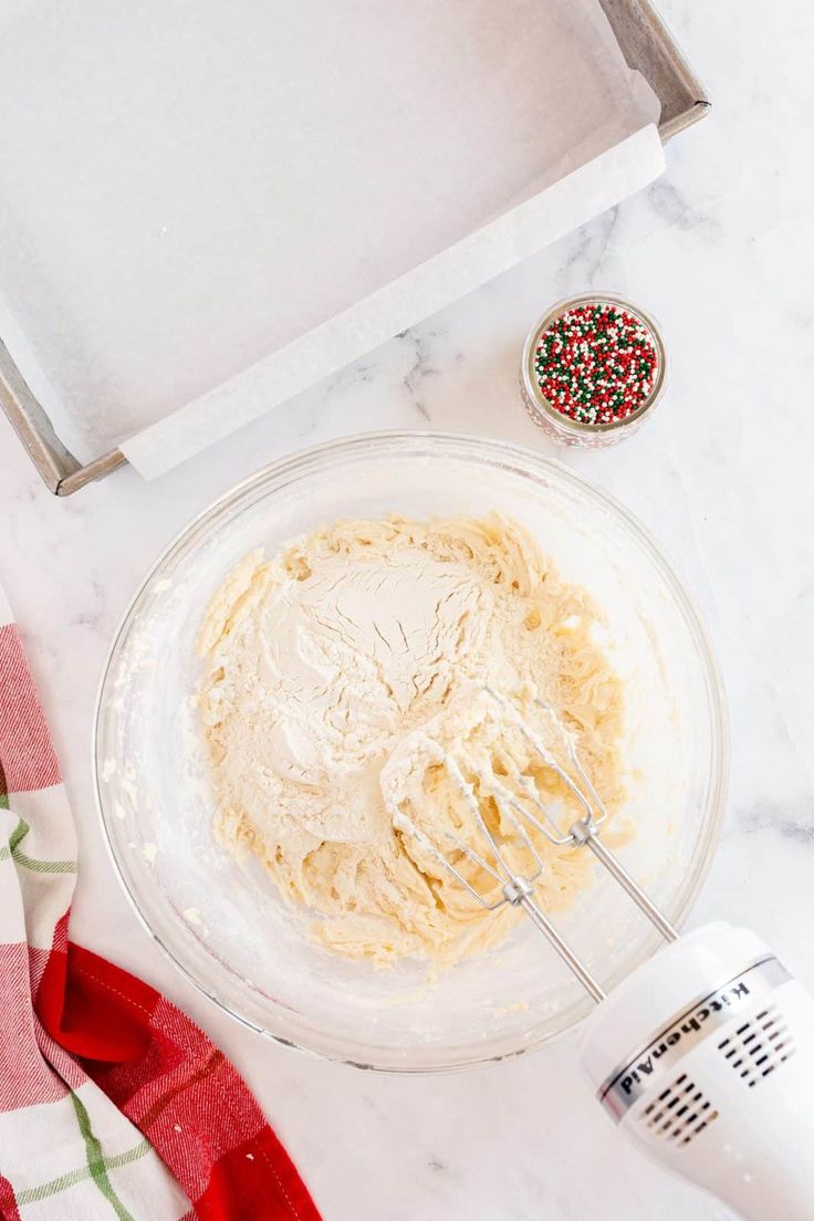 a bowl with some food in it next to a whisk and a mixer