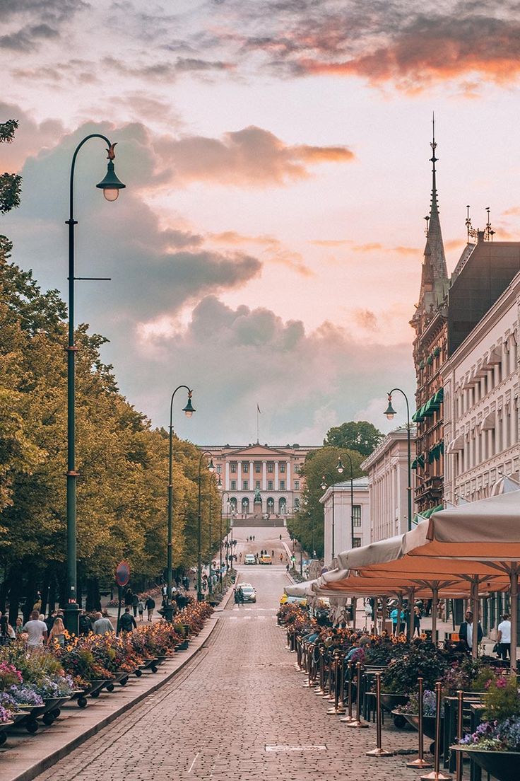 an empty city street with tables and umbrellas on both sides, during the sunset