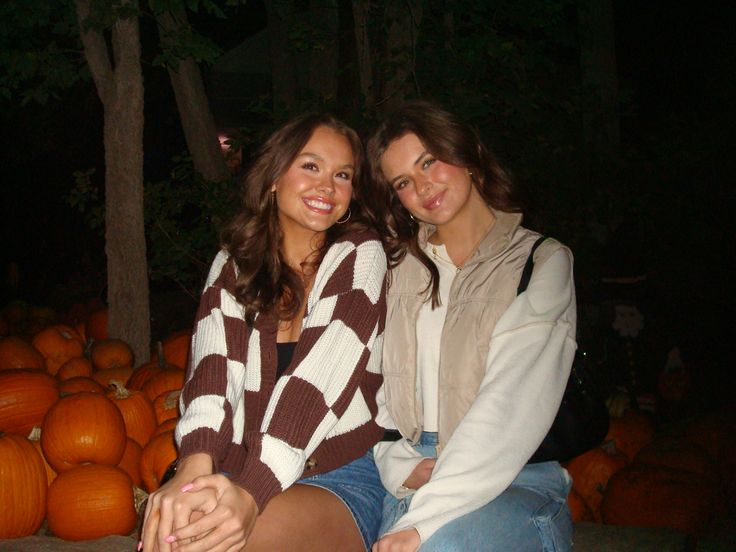 two young women sitting on top of each other in front of pumpkins at night