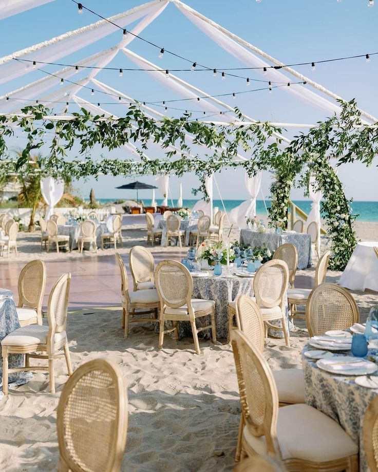 tables and chairs are set up on the beach for an outdoor wedding reception with white draping