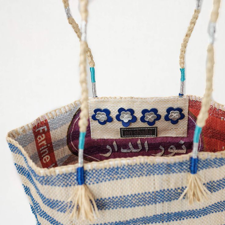 The Blue Stripe Market Bag by EnShallah is re-purposing with style! Made from a recycled grain bag that is re-imagined with color and hand embroidery by local women in villages outside of Marrakech, Morocco. The grain bag is turned inside out so the original design of the grain bag is on the inside, as a reminder of its original purpose. It is then hand embroidered using various materials and colors in bold graphic patterns. Each bag takes approximately three days to make. The natural strength o Blue Bucket Shoulder Bag For Market, Handmade Blue Beach Bag For Market, Blue Bucket Bags For Market, Blue Handwoven Shoulder Bag For Market, Artisan Blue Bags For Market, Blue Bucket Bag For Market, Artisan Blue Bag For Market, Blue Woven Bags For Market, Blue Fair Trade Bag For Daily Use