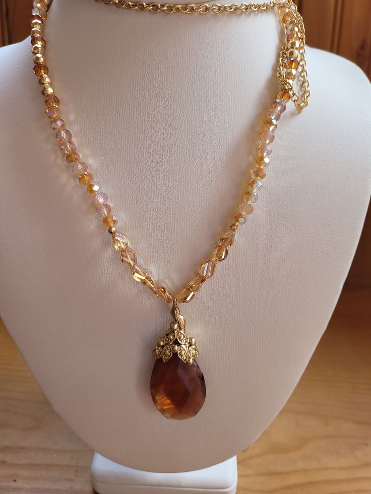 The necklace has a two inch pear cut reddish brown crystal stone decorated with a crystal accented leaf design.  The chain is 24 to 30 inches adjustable and is made of 4mm red and brown crystal beads.  Gold plate. Elegant Brown Beaded Necklaces With Gemstones, Elegant Amber Necklace With Beaded Chain, Elegant Amber Beaded Necklace With Stones, Elegant Brown Beaded Necklace With Gemstone, Elegant Amber Crystal Necklace With Stones, Elegant Gold Beaded Necklace With Teardrop Pendant, Elegant Beaded Teardrop Pendant Crystal Necklace, Elegant Amber Beaded Chain Necklace, Elegant Red Crystal Necklaces With Natural Stones