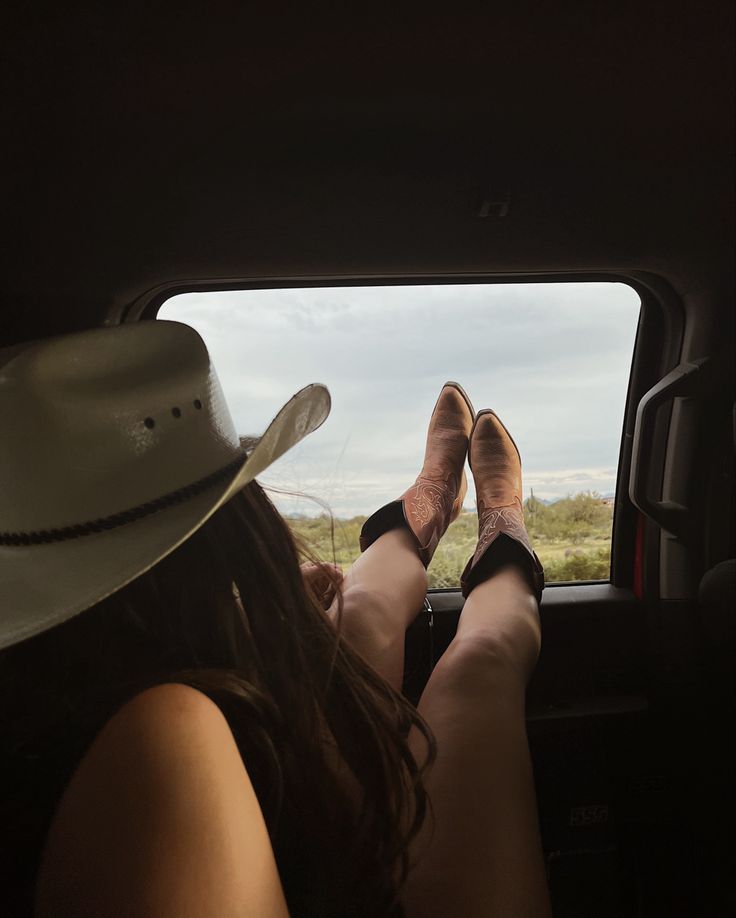 a woman sitting in the back seat of a car with her legs crossed and wearing cowboy hats