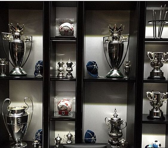 many trophies are displayed on shelves in a room with black leather chairs and dark walls