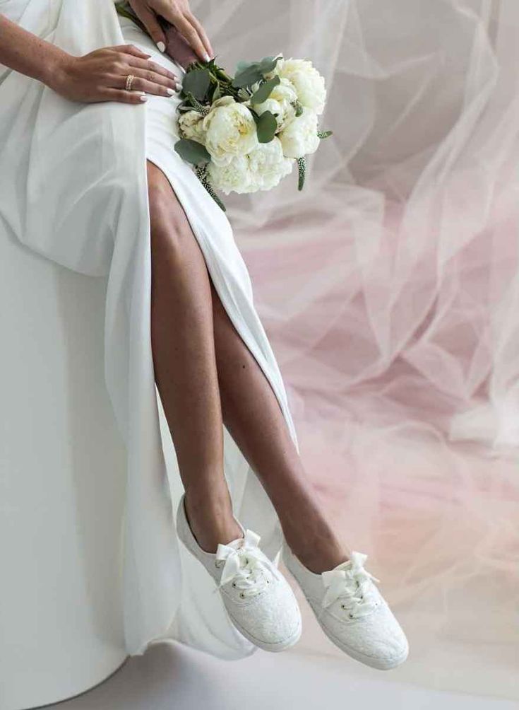 a woman in white shoes is sitting on a chair with her legs crossed and holding flowers