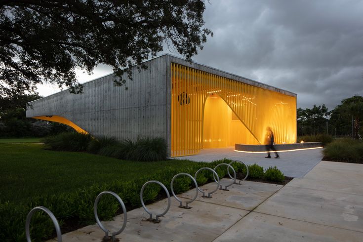 a person walking past a building with yellow lights on it's side and some metal bars in the foreground