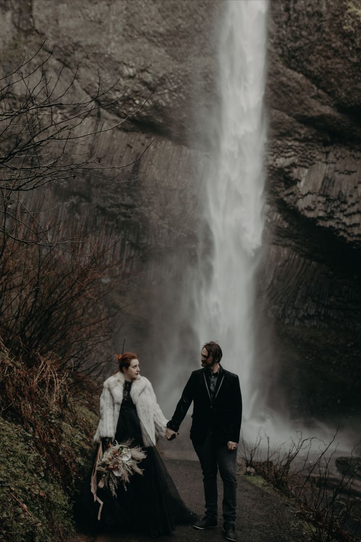 a man and woman holding hands in front of a waterfall