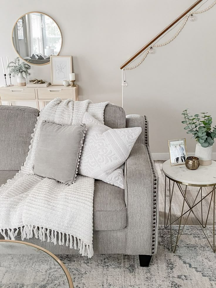 a living room with a gray couch and white pillows on top of the couch is next to a round coffee table